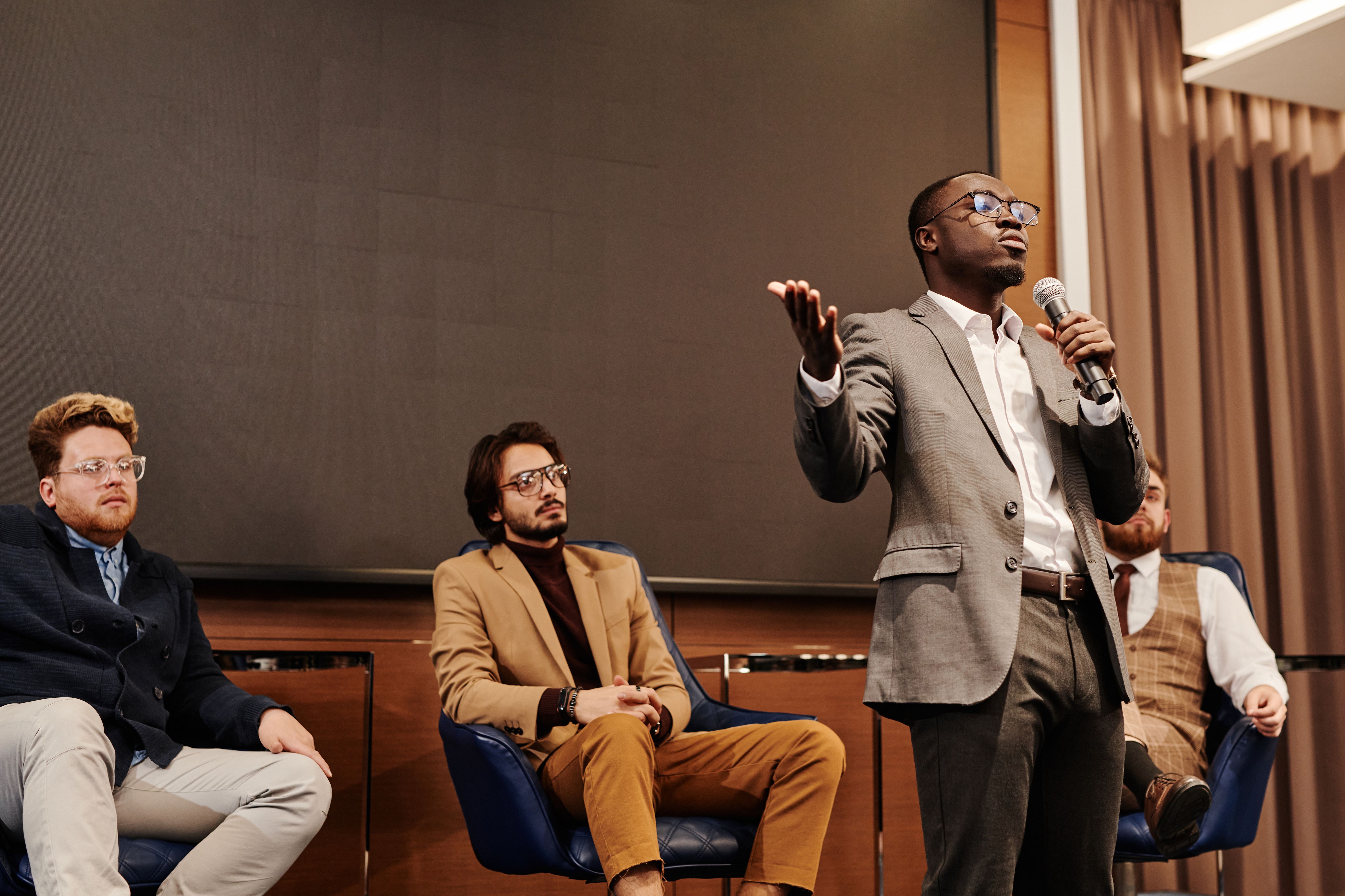 A speaker addressing an audience with a microphone on a panel.